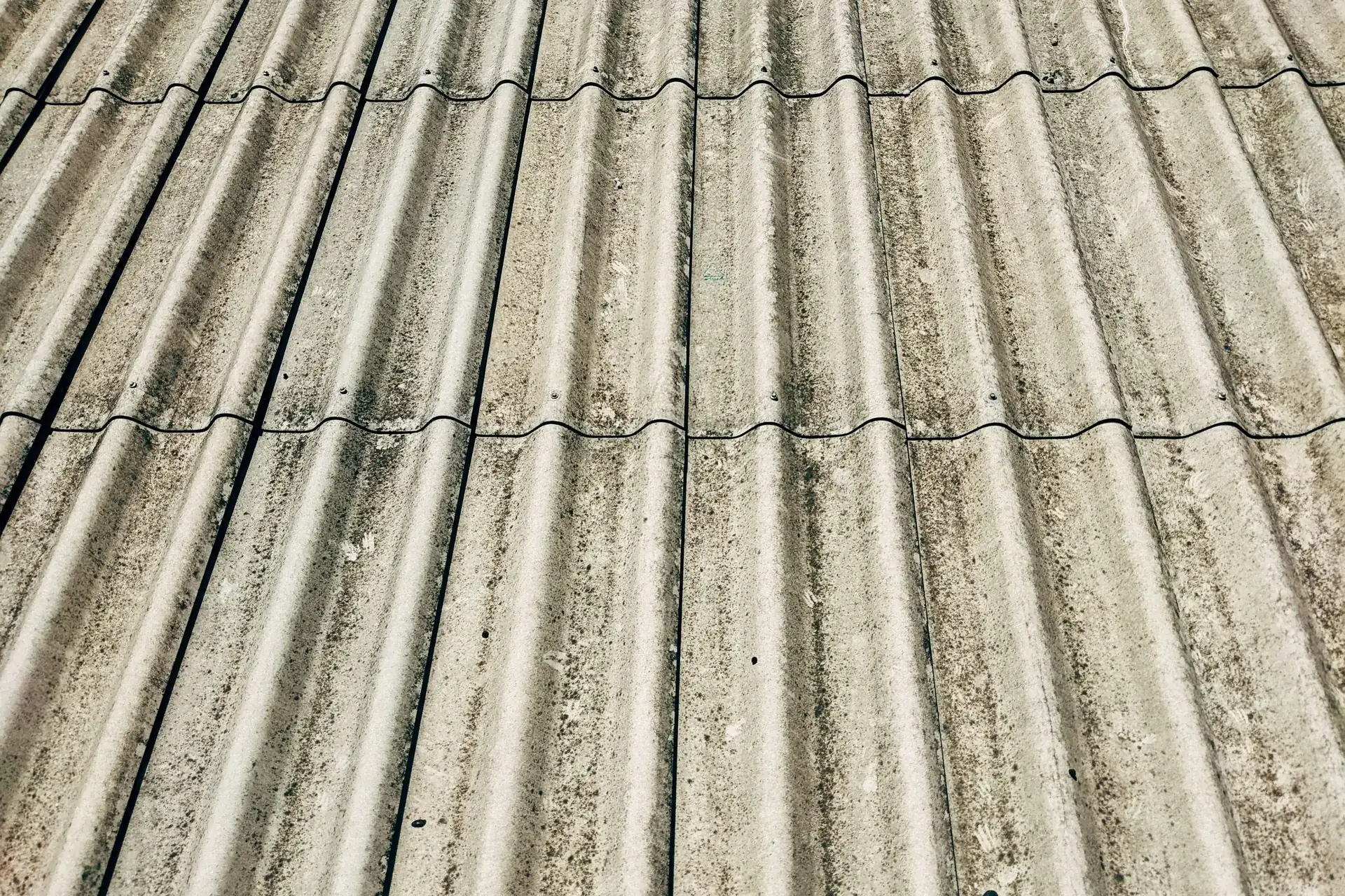 Verweerde golfplaten van asbestcement op het dak van een bedrijfshal