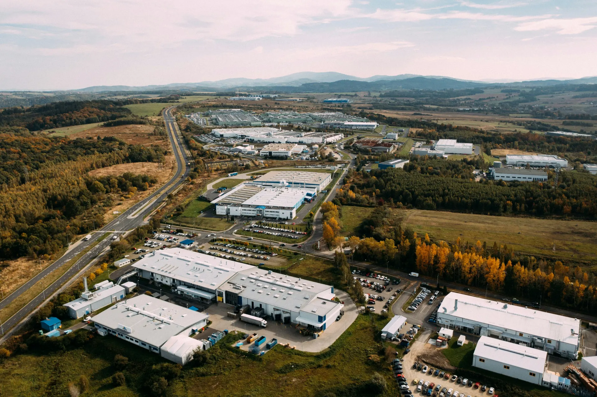 Vue aérienne d'une zone industrielle avec des toitures plates sur des halls de production et des entrepôts, entre des bois aux couleurs d'automne