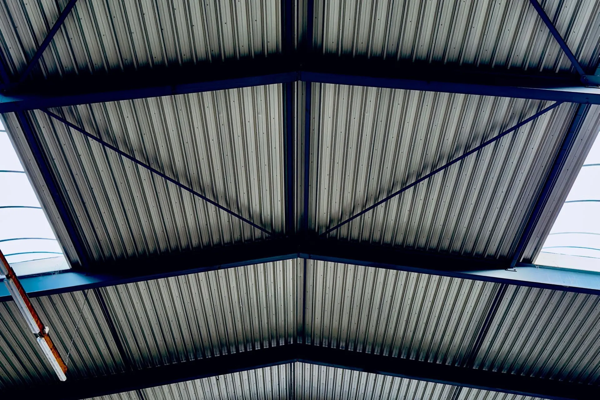 Toiture steeldeck vue de dessous : bacs acier profilés sur les poutres et contreventements en acier bleu d'un hall industriel